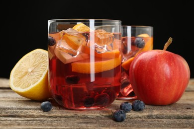 Photo of Tasty punch in glasses and fresh fruits on wooden table against black background, closeup. Refreshing drink