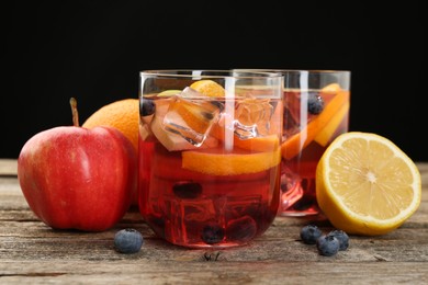 Photo of Tasty punch in glasses and fresh fruits on wooden table against black background, closeup. Refreshing drink