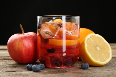 Photo of Tasty punch in glass and fresh fruits on wooden table against black background, closeup. Refreshing drink