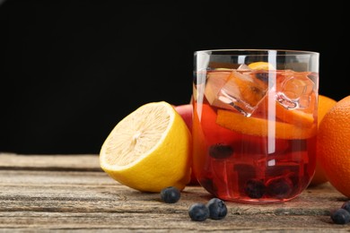 Photo of Tasty punch in glass and fresh fruits on wooden table against black background, closeup. Refreshing drink