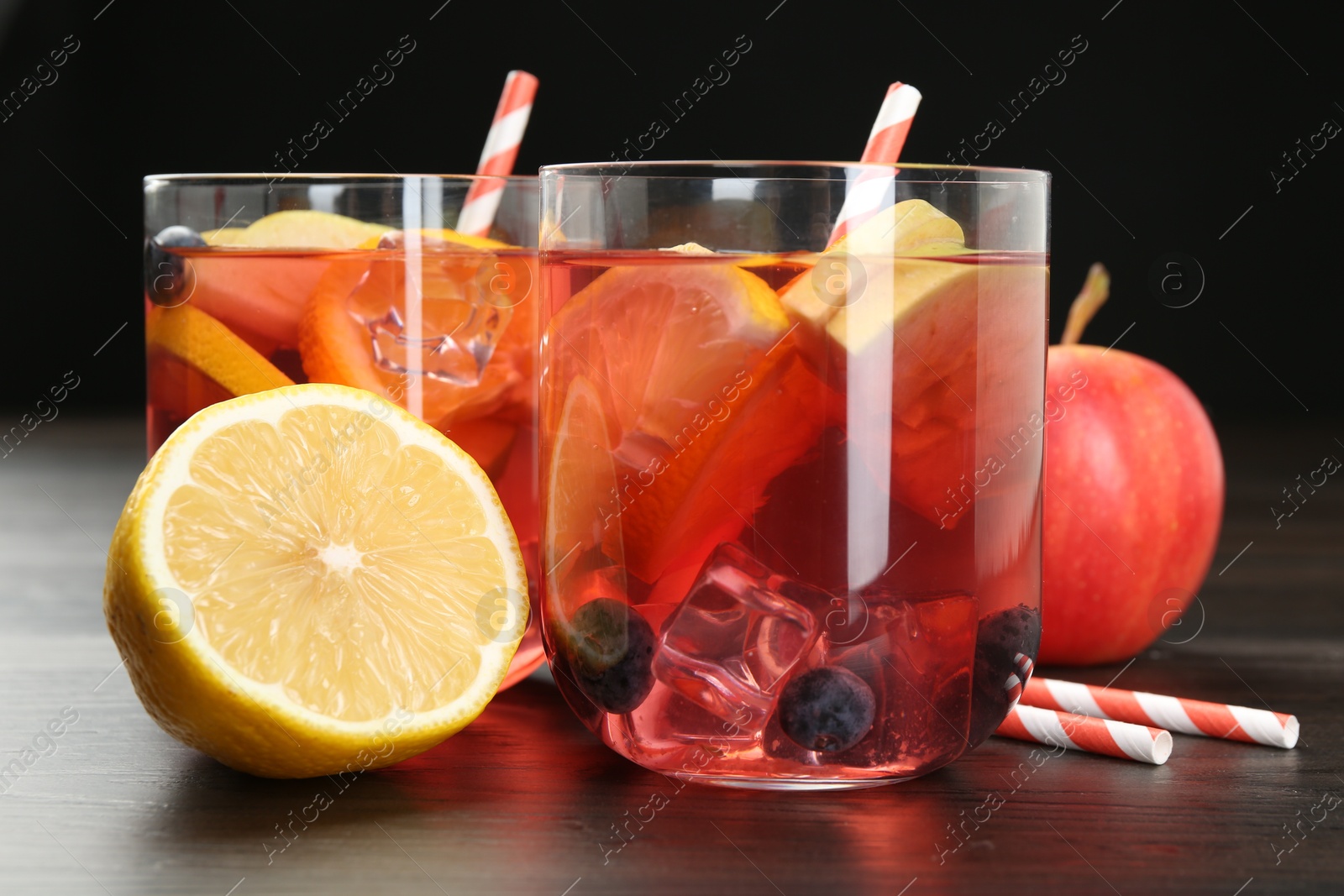 Photo of Tasty punch in glasses and fresh fruits on wooden table against black background, closeup. Refreshing drink