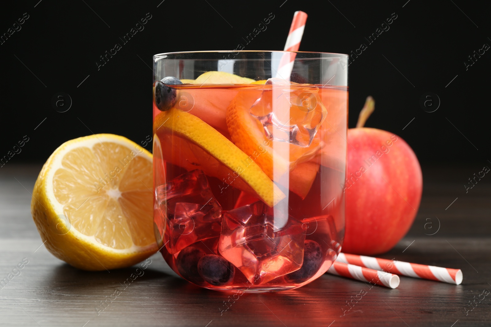 Photo of Tasty punch in glass and fresh fruits on wooden table against black background, closeup. Refreshing drink