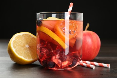 Photo of Tasty punch in glass and fresh fruits on wooden table against black background, closeup. Refreshing drink