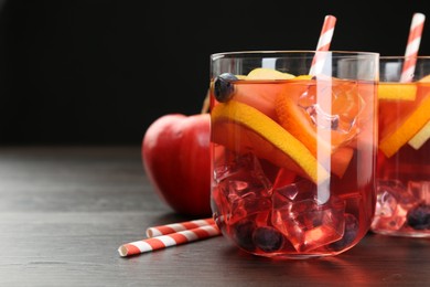 Photo of Tasty punch in glasses and fresh fruit on wooden table against black background, closeup. Refreshing drink