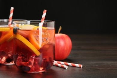Photo of Tasty punch in glasses and fresh fruit on wooden table against black background, closeup. Refreshing drink