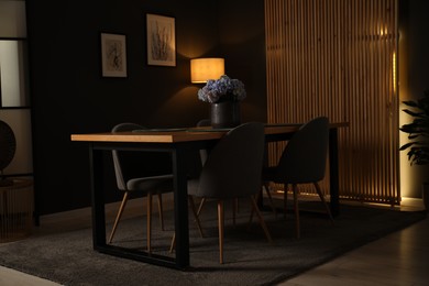 Photo of Wooden table with beautiful flowers and chairs in dining room at night