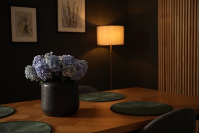 Photo of Wooden table with beautiful flowers in dining room at night, closeup
