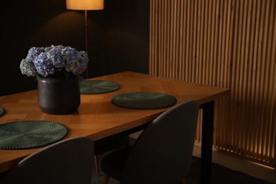 Photo of Wooden table with beautiful flowers and chairs in dining room at night