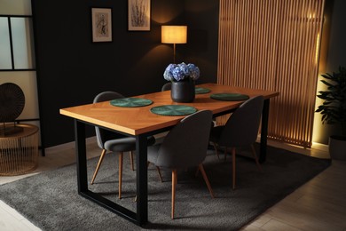 Photo of Wooden table with beautiful flowers and chairs in dining room at night