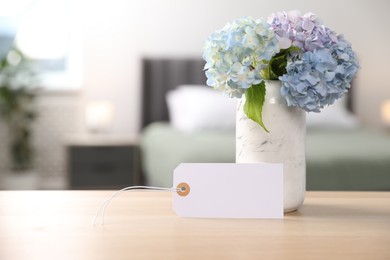 Photo of Empty card and hydrangea flowers on wooden table in hotel room. Space for text