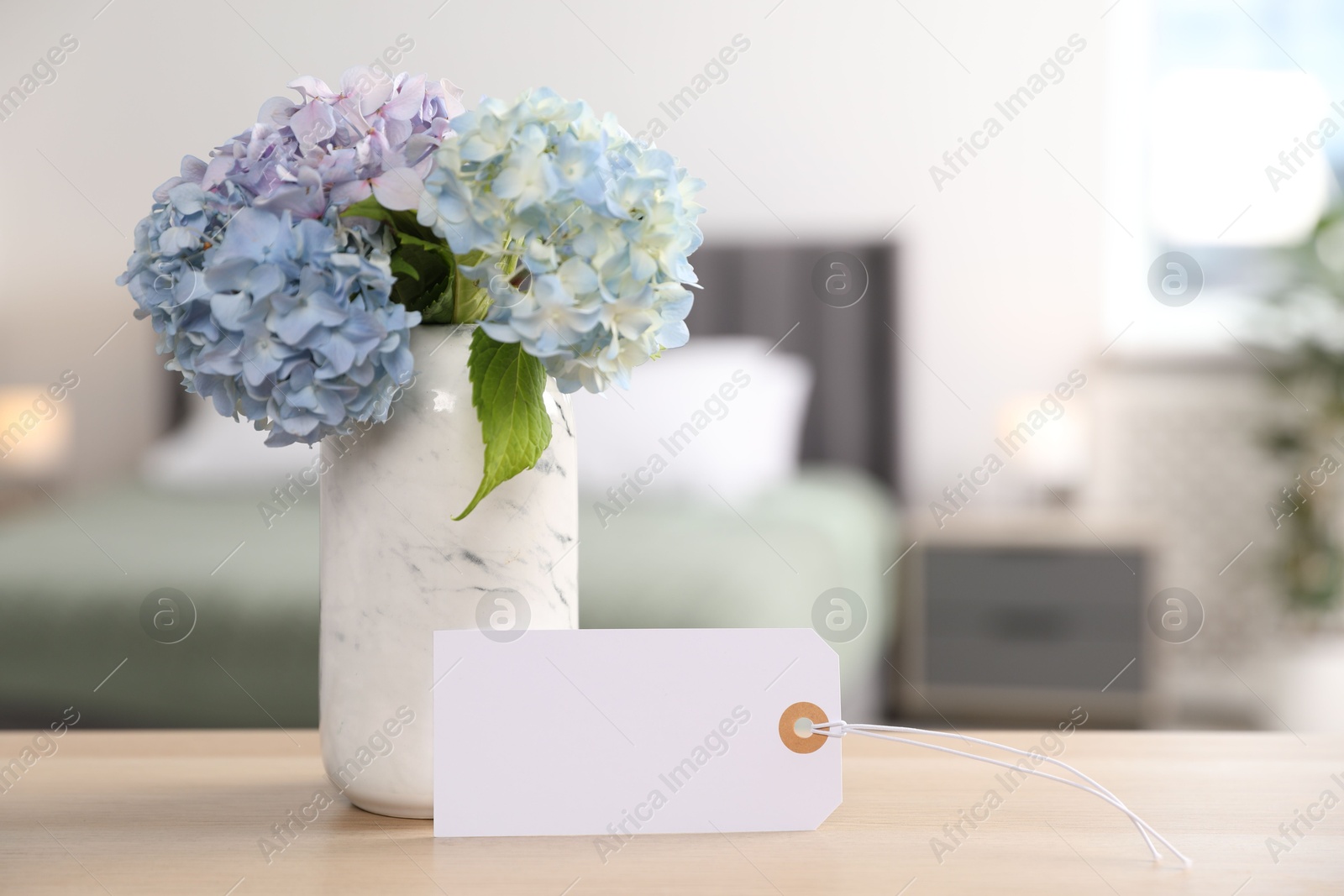 Photo of Empty card and hydrangea flowers on wooden table in hotel room. Space for text
