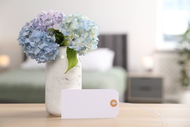 Photo of Empty card and hydrangea flowers on wooden table in hotel room. Space for text