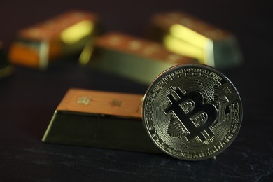 Photo of Cryptocurrency. One golden bitcoin and gold bars on black table, closeup