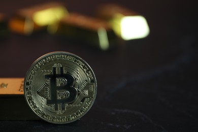 Photo of Cryptocurrency. One golden bitcoin and gold bars on black table, closeup. Space for text