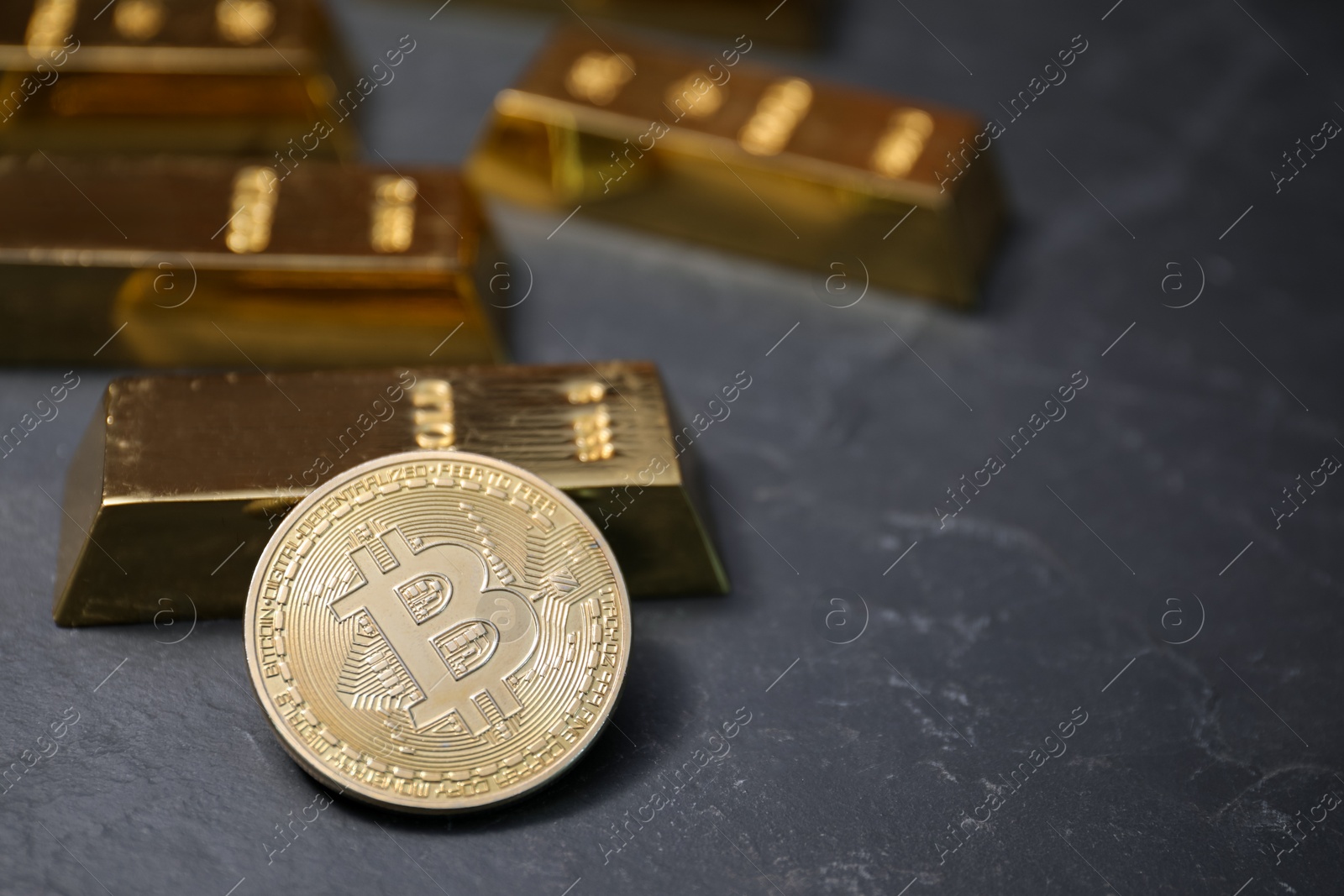 Photo of Cryptocurrency. One golden bitcoin and gold bars on black table, closeup. Space for text
