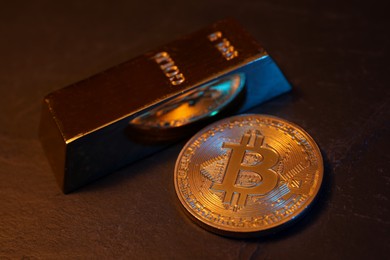 Photo of Cryptocurrency. One golden bitcoin and gold bar on black table, closeup