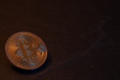 Photo of Cryptocurrency. One golden bitcoin on black table, closeup. Space for text