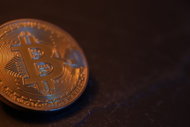 Photo of Cryptocurrency. One golden bitcoin on black table, closeup. Space for text