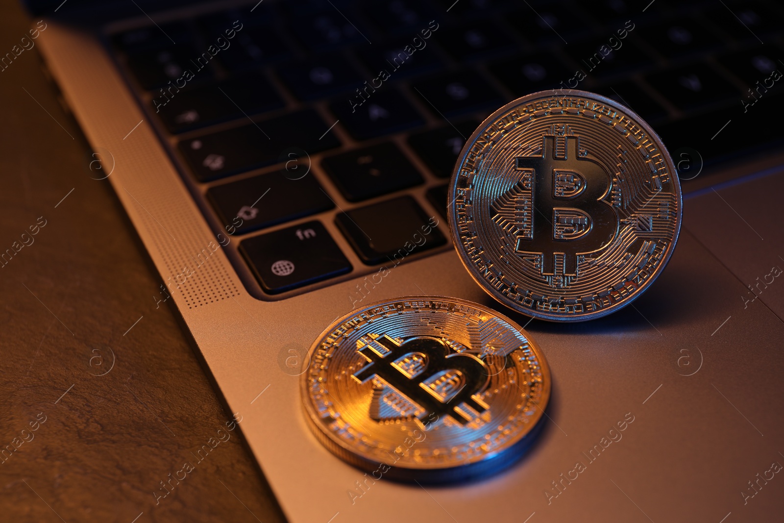 Photo of Cryptocurrency. Silver bitcoins and laptop on black table, closeup. Space for text