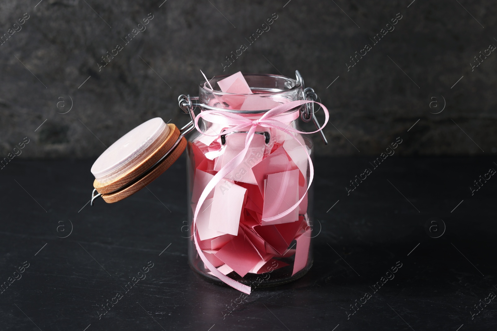 Pink paper pieces in glass jar on black table. Notes with messages Photo of Pink paper pieces in glass jar on black table. Notes with messages