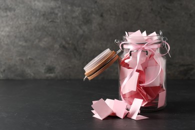 Photo of Pink paper pieces in glass jar on black table, space for text. Notes with messages