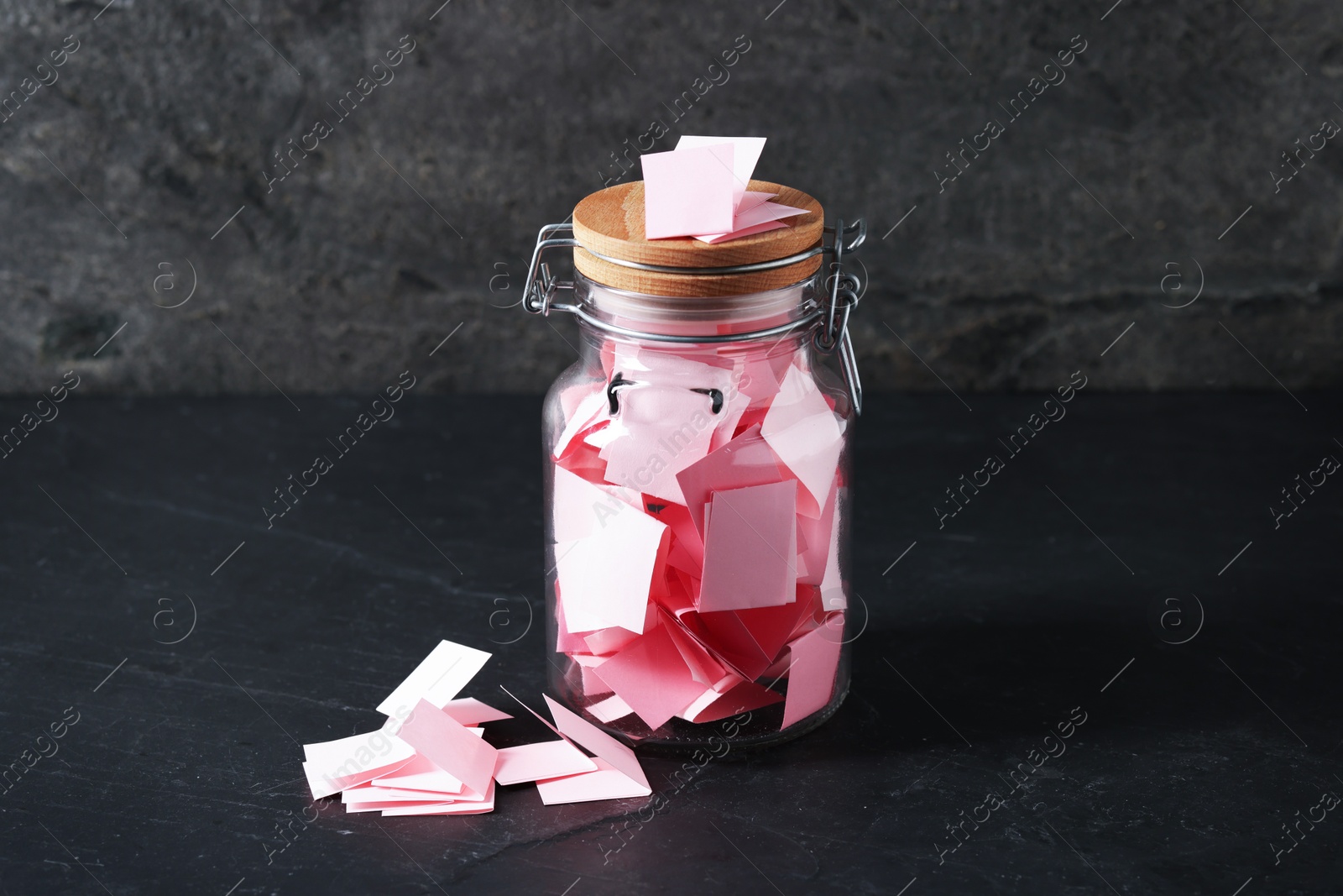 Pink paper pieces in glass jar on black table. Notes with messages Photo of Pink paper pieces in glass jar on black table. Notes with messages