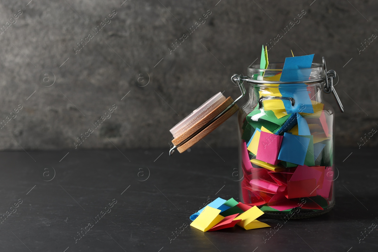 Colorful paper pieces in glass jar on black table, space for text. Notes with messages Photo of Colorful paper pieces in glass jar on black table, space for text. Notes with messages