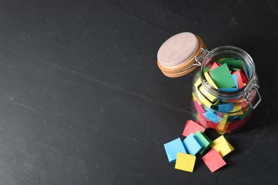 Photo of Colorful paper pieces in glass jar on black table, above view. Space for text. Notes with messages