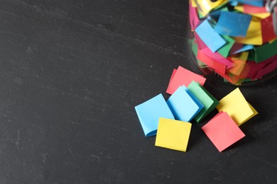 Photo of Colorful paper pieces in glass jar on black table, above view. Space for text. Notes with messages
