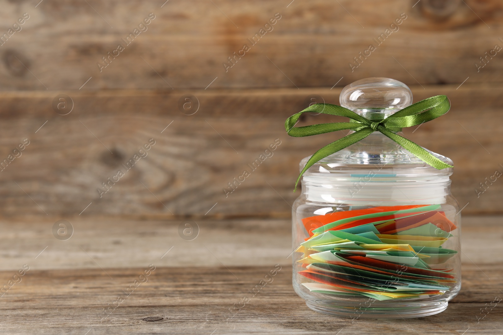 Colorful paper pieces in glass jar on wooden table, closeup. Space for text. Notes with messages Photo of Colorful paper pieces in glass jar on wooden table, closeup. Space for text. Notes with messages