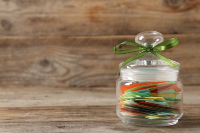Photo of Colorful paper pieces in glass jar on wooden table, closeup. Space for text. Notes with messages