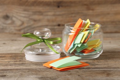 Photo of Colorful paper pieces in glass jar on wooden table, closeup. Notes with messages
