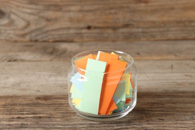 Photo of Colorful paper pieces in glass jar on wooden table, closeup. Notes with messages