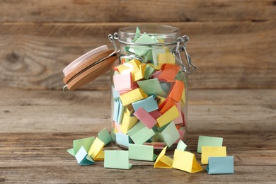 Photo of Colorful paper pieces in glass jar on wooden table. Notes with messages