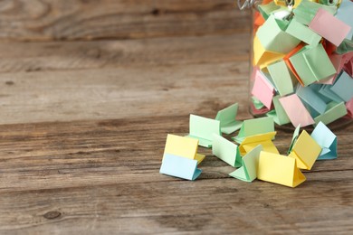Photo of Colorful paper pieces in glass jar on wooden table, closeup. Space for text. Notes with messages