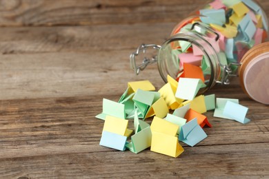Photo of Colorful paper pieces in glass jar on wooden table, closeup. Space for text. Notes with messages