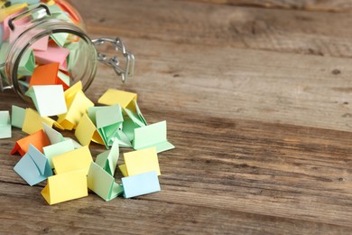 Photo of Colorful paper pieces in glass jar on wooden table, closeup. Space for text. Notes with messages