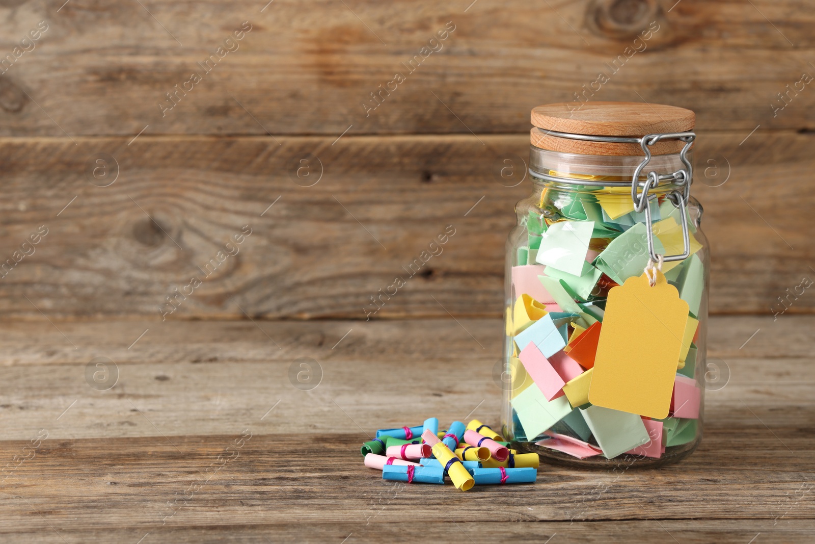 Colorful paper pieces in glass jar on wooden table, space for text. Notes with messages Photo of Colorful paper pieces in glass jar on wooden table, space for text. Notes with messages