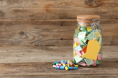 Photo of Colorful paper pieces in glass jar on wooden table, space for text. Notes with messages