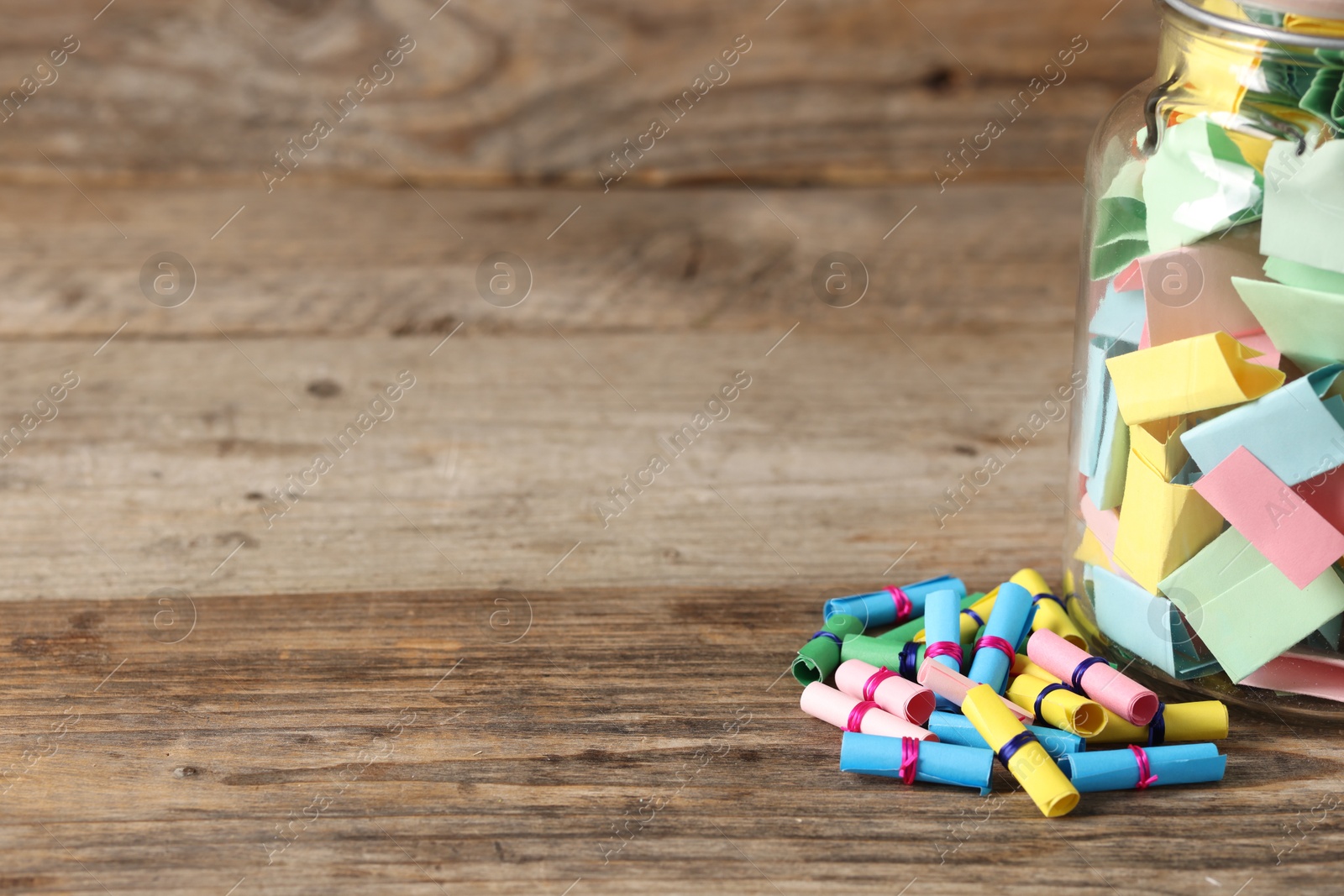 Colorful paper pieces in glass jar on wooden table, closeup. Space for text. Notes with messages Photo of Colorful paper pieces in glass jar on wooden table, closeup. Space for text. Notes with messages