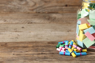 Photo of Colorful paper pieces in glass jar on wooden table, closeup. Space for text. Notes with messages