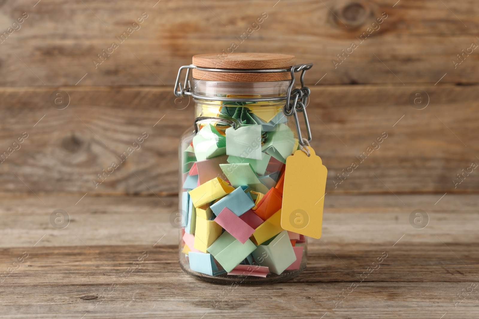 Colorful paper pieces in glass jar on wooden table. Notes with messages Photo of Colorful paper pieces in glass jar on wooden table. Notes with messages