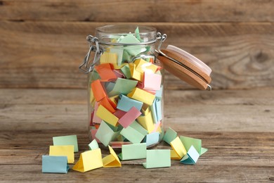 Photo of Colorful paper pieces in glass jar on wooden table. Notes with messages