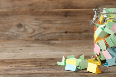 Photo of Colorful paper pieces in glass jar on wooden table, closeup. Space for text. Notes with messages