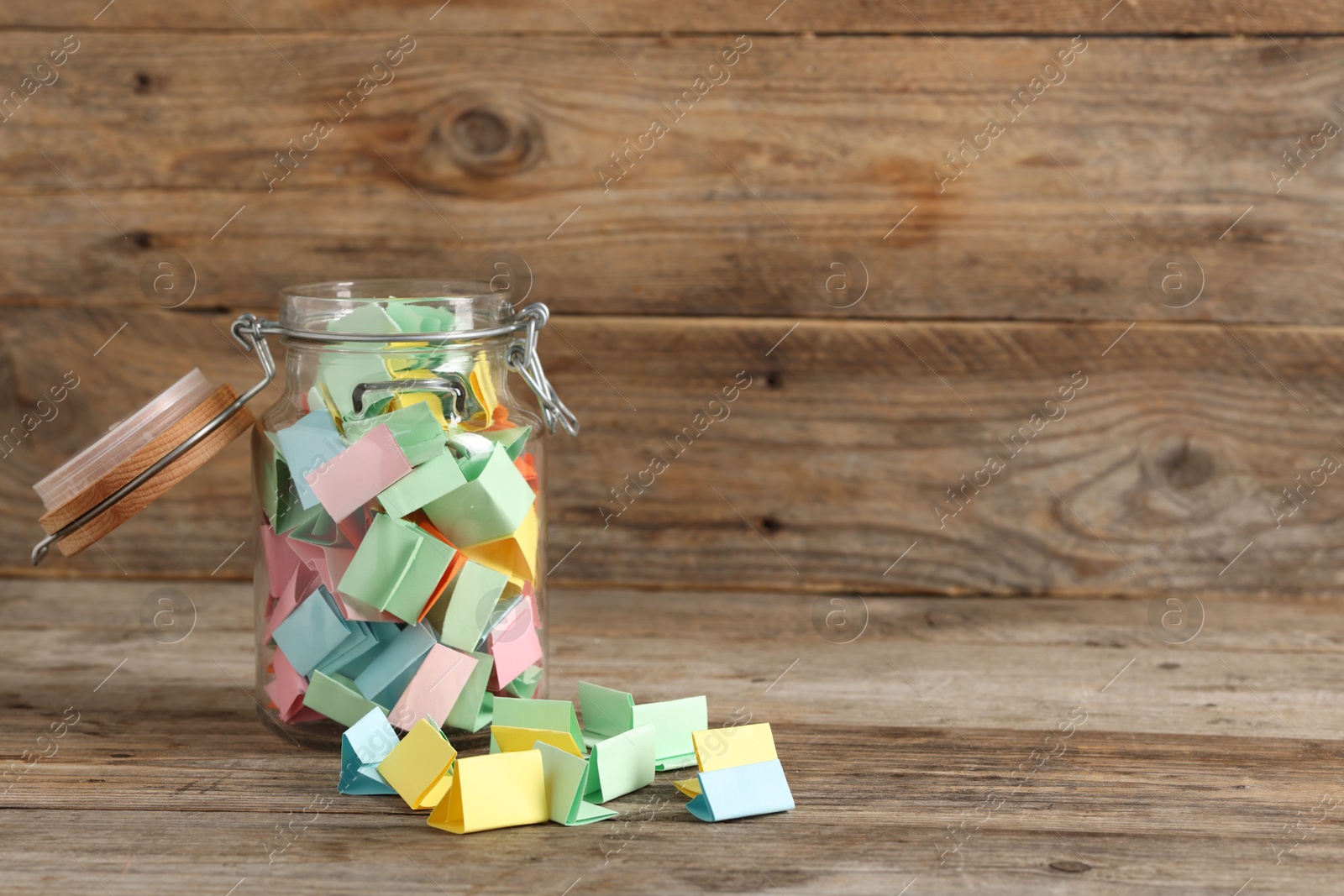 Colorful paper pieces in glass jar on wooden table, space for text. Notes with messages Photo of Colorful paper pieces in glass jar on wooden table, space for text. Notes with messages