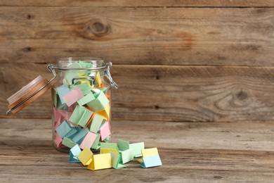 Photo of Colorful paper pieces in glass jar on wooden table, space for text. Notes with messages