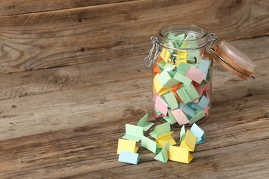 Photo of Colorful paper pieces in glass jar on wooden table, space for text. Notes with messages