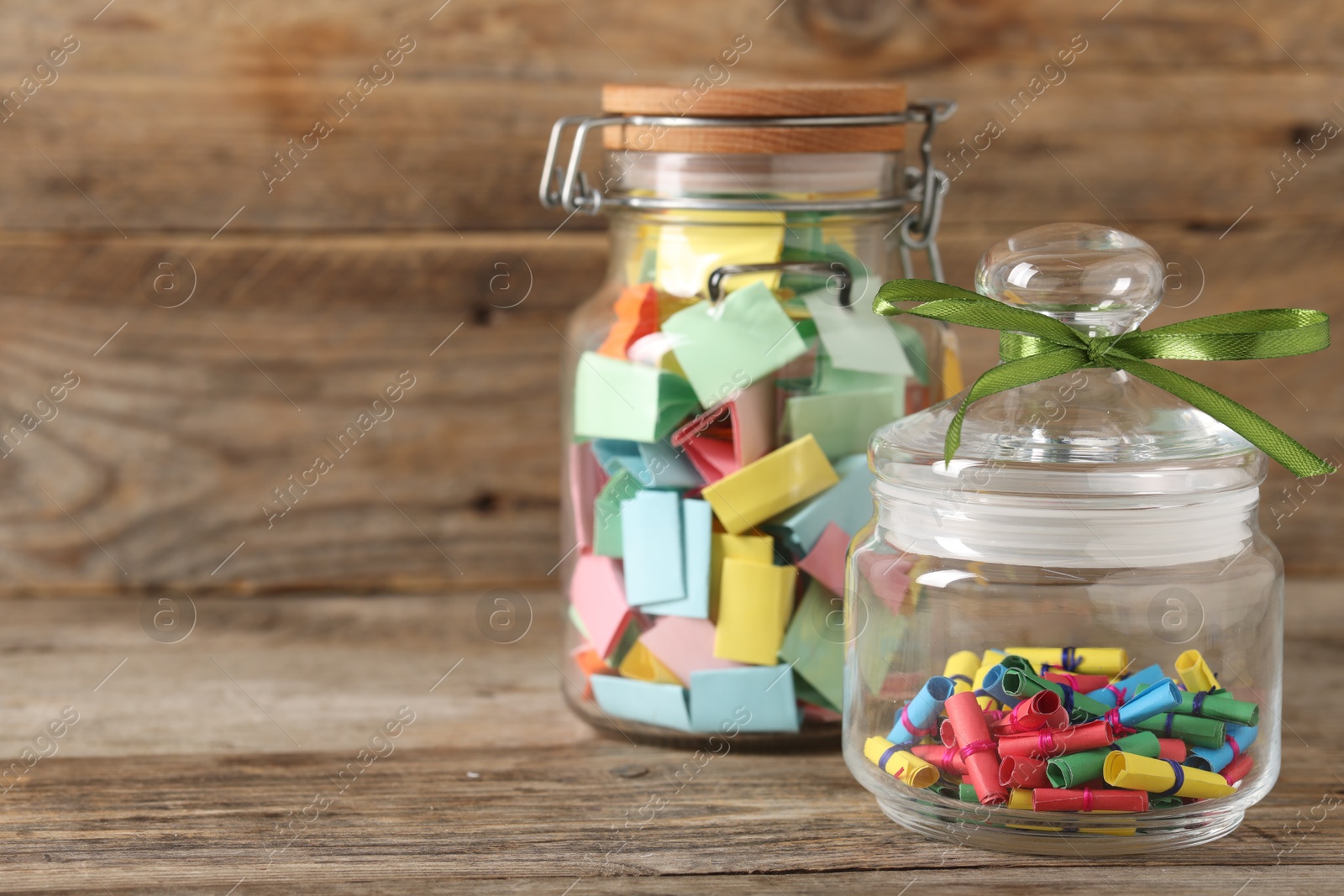 Colorful paper pieces in glass jars on wooden table, closeup. Space for text. Notes with messages Photo of Colorful paper pieces in glass jars on wooden table, closeup. Space for text. Notes with messages