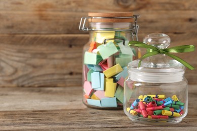 Photo of Colorful paper pieces in glass jars on wooden table, closeup. Space for text. Notes with messages