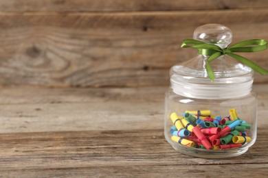 Photo of Colorful paper pieces in glass jar on wooden table, closeup. Space for text. Notes with messages